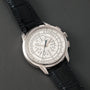 The Patek Philippe Multi-Scale Chronograph, featuring a black leather strap and intricate silver dial, is elegantly displayed on a dark surface.