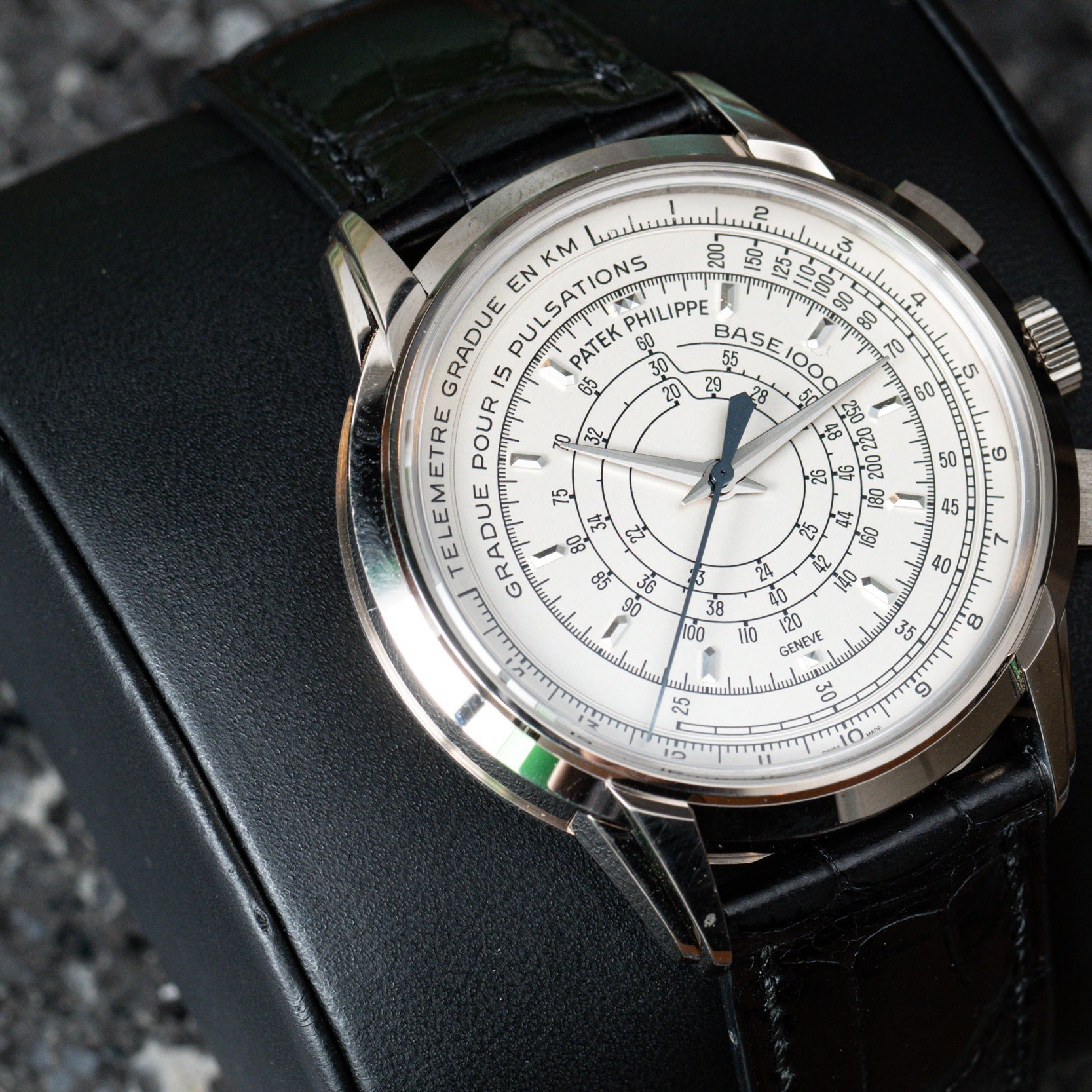 The Patek Philippe Multi-Scale Chronograph wristwatch with a black leather strap is displayed on a black cushion.