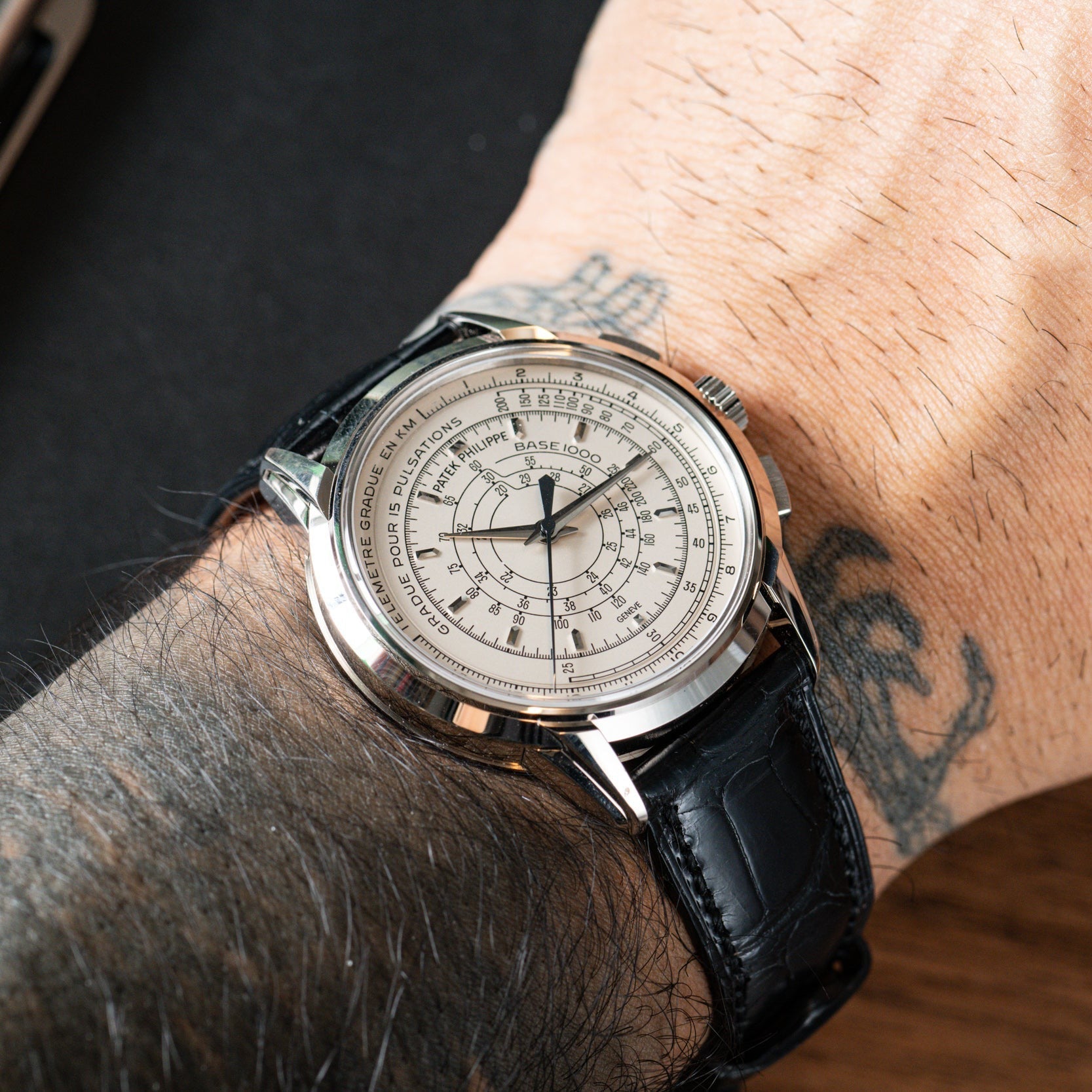 A close-up of the Patek Philippe Multi-Scale Chronograph with a black leather strap, showcased on a tattooed wrist.