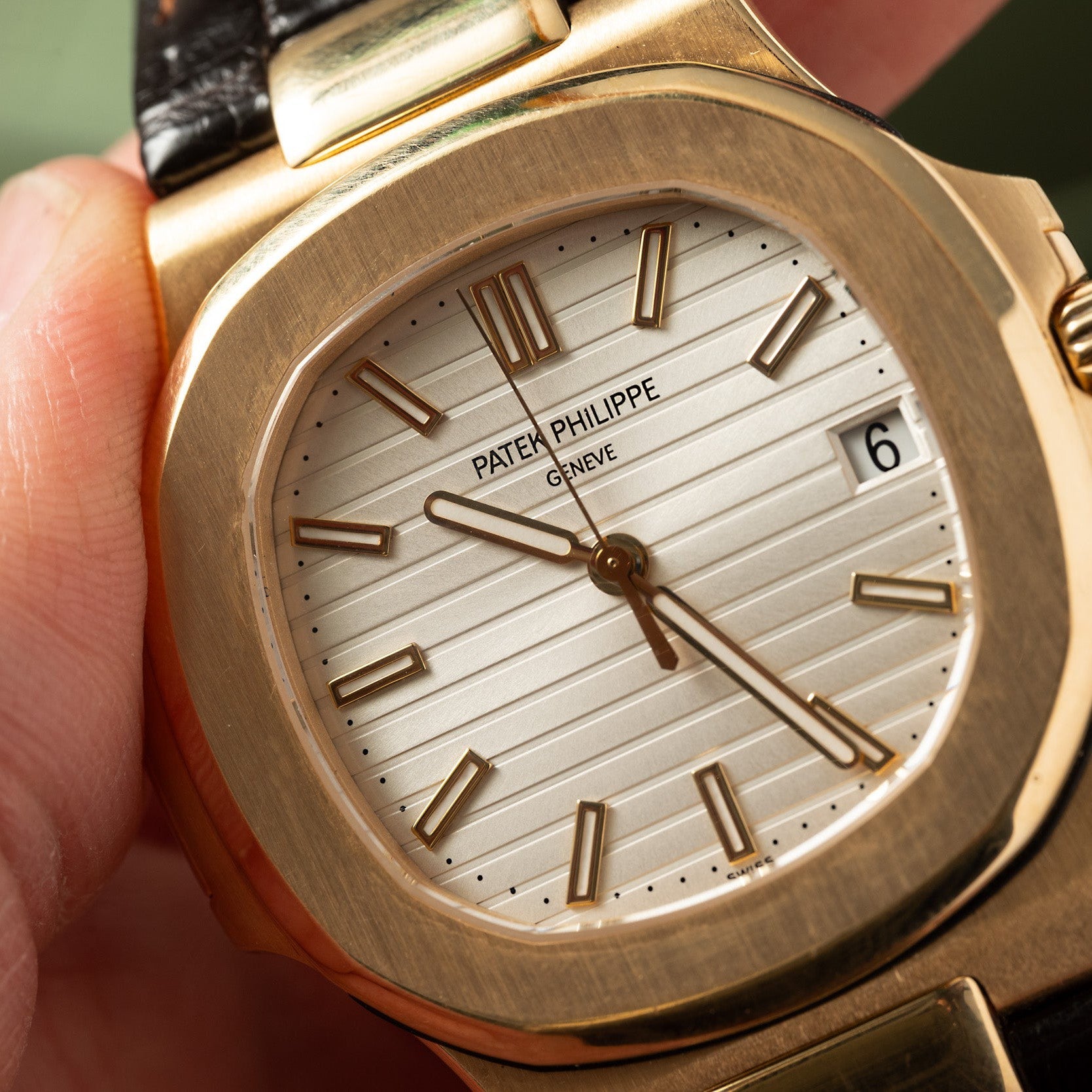 Close-up of a Patek Philippe Nautilus wristwatch with a gold case, white dial, and black leather strap, displaying the date 6.