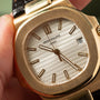Close-up of a Patek Philippe Nautilus wristwatch with a gold case, white dial, and black leather strap, displaying the date 6.