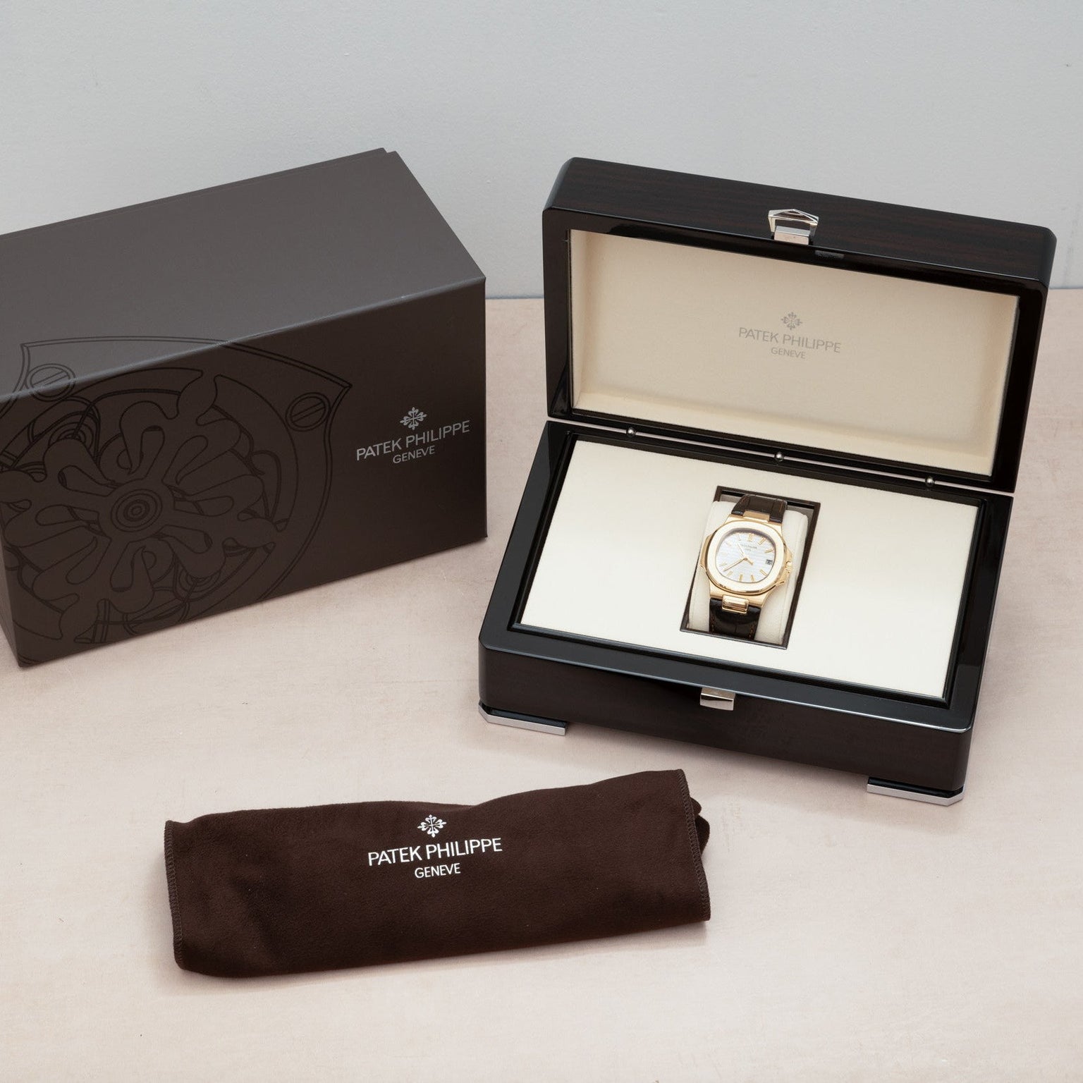 A Patek Philippe Nautilus watch in an open display box, next to a branded case and brown cloth pouch.