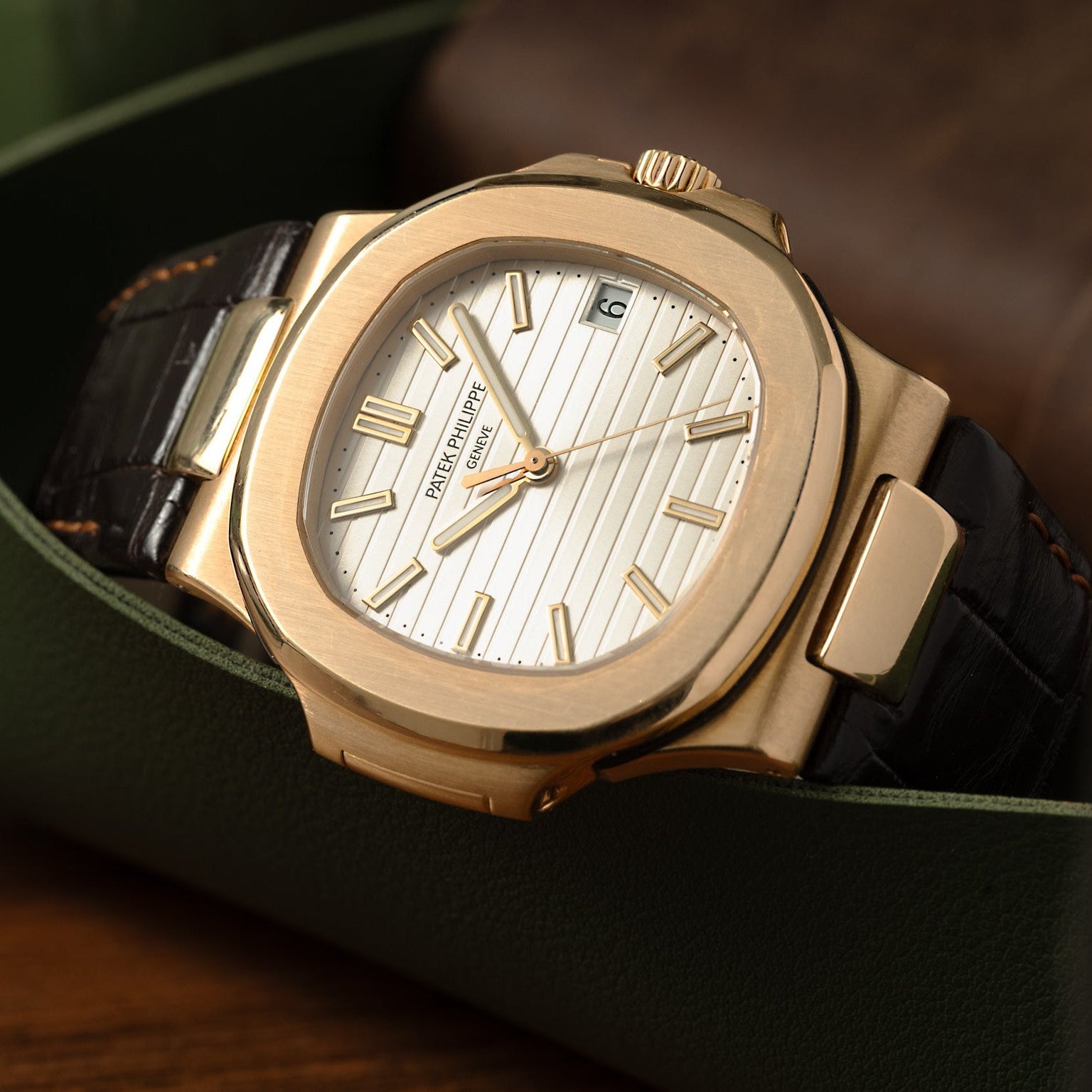 A Patek Philippe Nautilus wristwatch with a white dial and black leather strap is displayed in a green case.