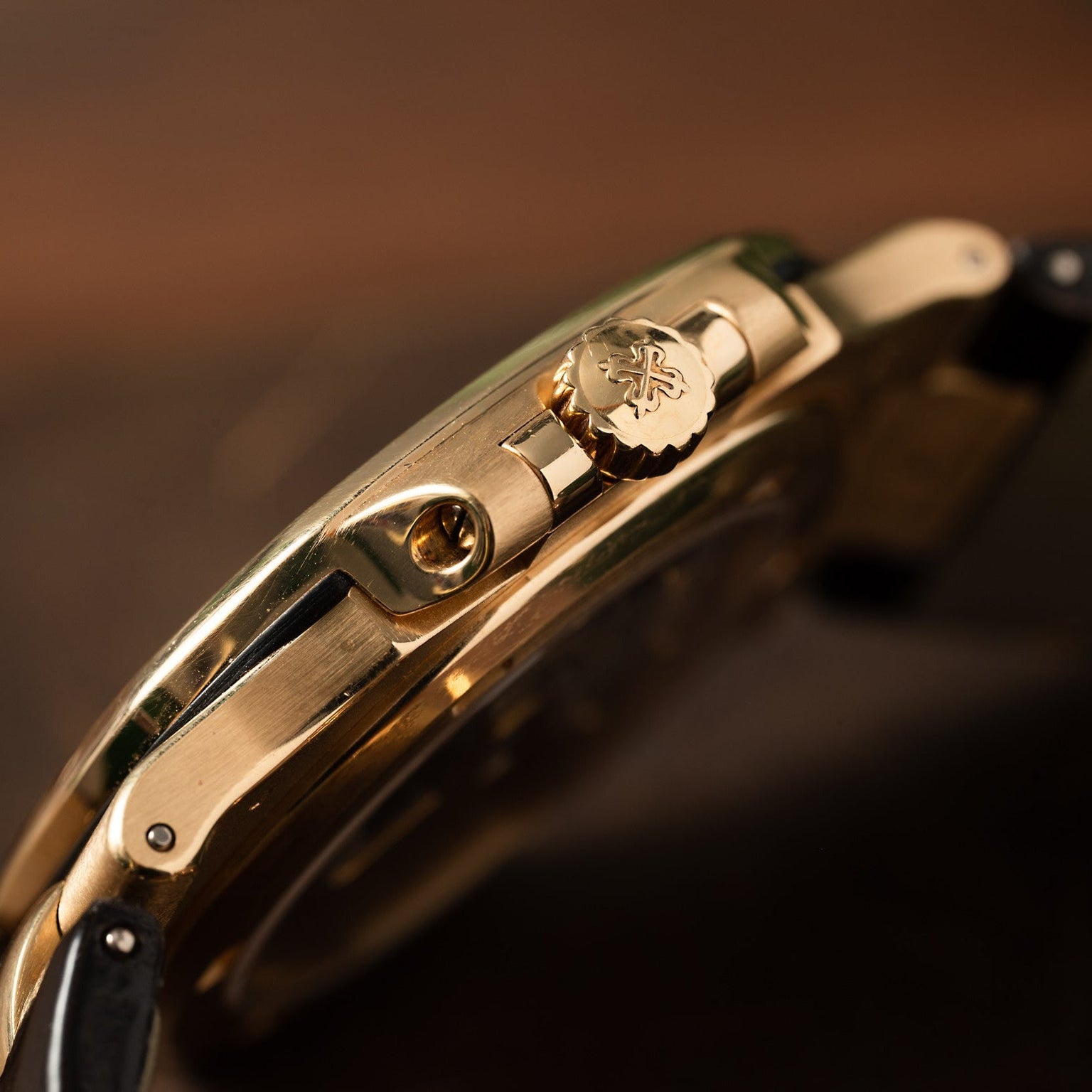 Close-up side view of the Patek Philippe Nautilus gold wristwatch featuring a crown engraved with a decorative emblem.