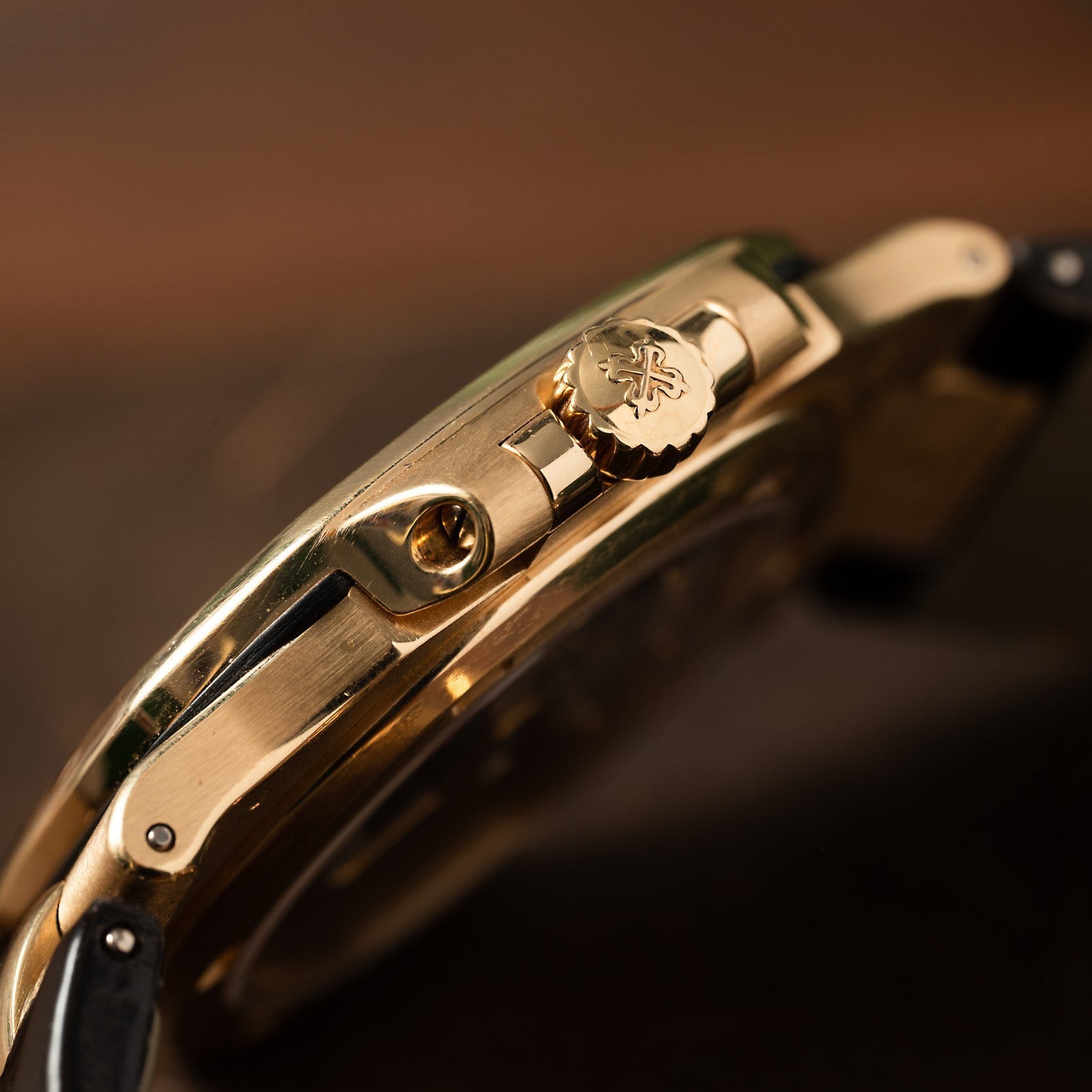 Close-up side view of the Patek Philippe Nautilus gold wristwatch featuring a crown engraved with a decorative emblem.