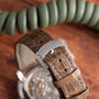 Close-up of a brown leather strap with a diamond-studded clasp on a wooden surface, featuring the Patek Philippe Ladies Complication watch.