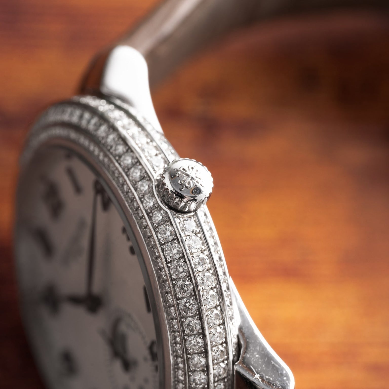 Close-up of the Patek Philippe Ladies Complication watch with a diamond-studded bezel and ornate crown, displayed on a wooden surface.