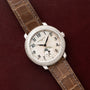 The Patek Philippe Ladies Complication watch, featuring a brown leather strap, is displayed on a dark red surface.