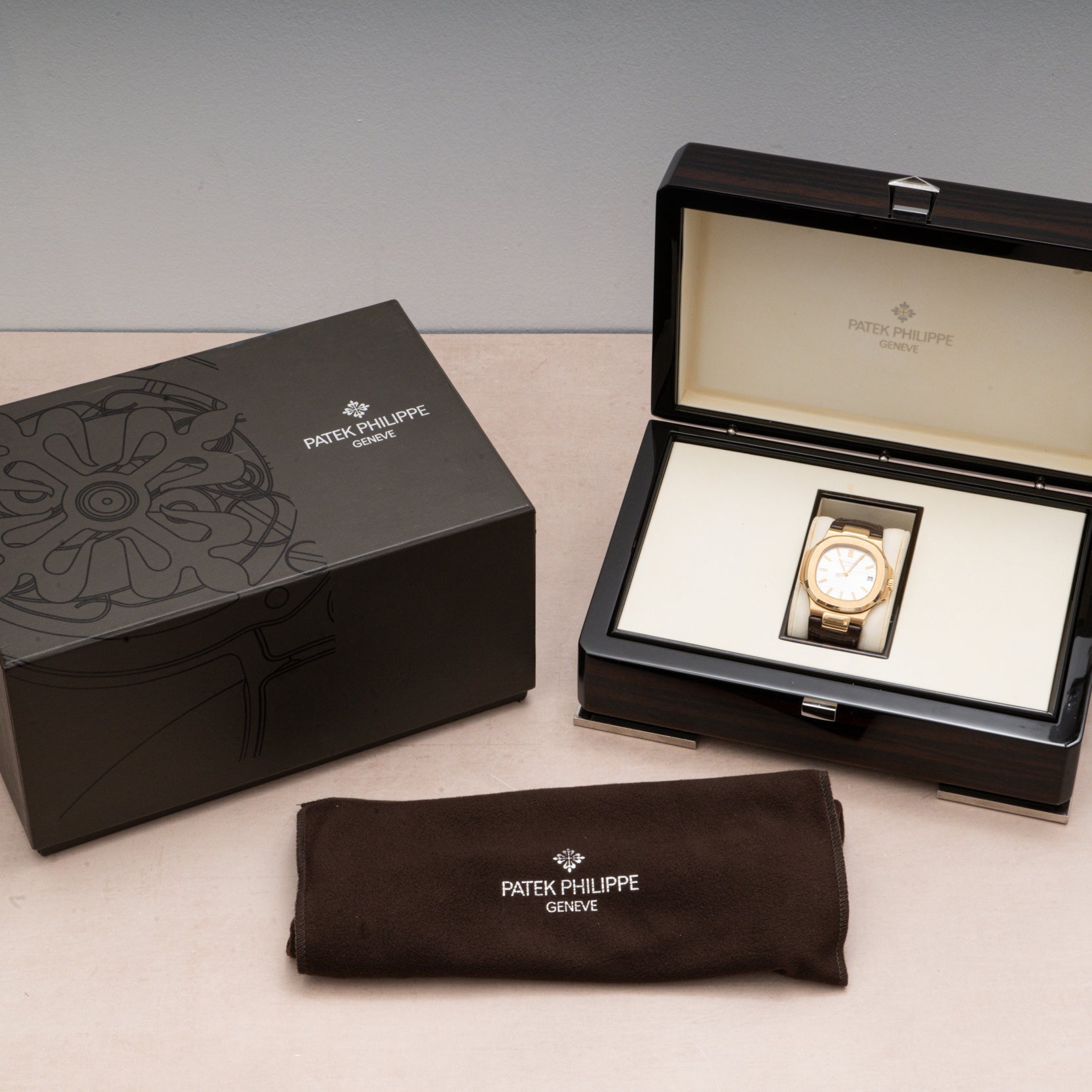 A Patek Philippe Nautilus watch displayed in an open box, accompanied by its outer box and a branded cloth.