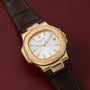 Patek Philippe Nautilus watch with white dial and brown leather strap on a dark red surface.