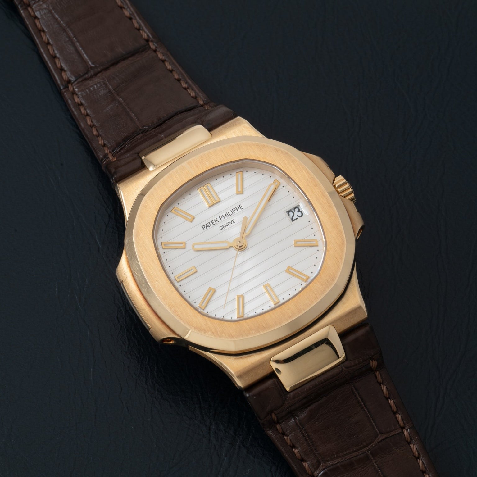 Patek Philippe Nautilus watch featuring a white dial and brown leather strap displayed on a dark surface.