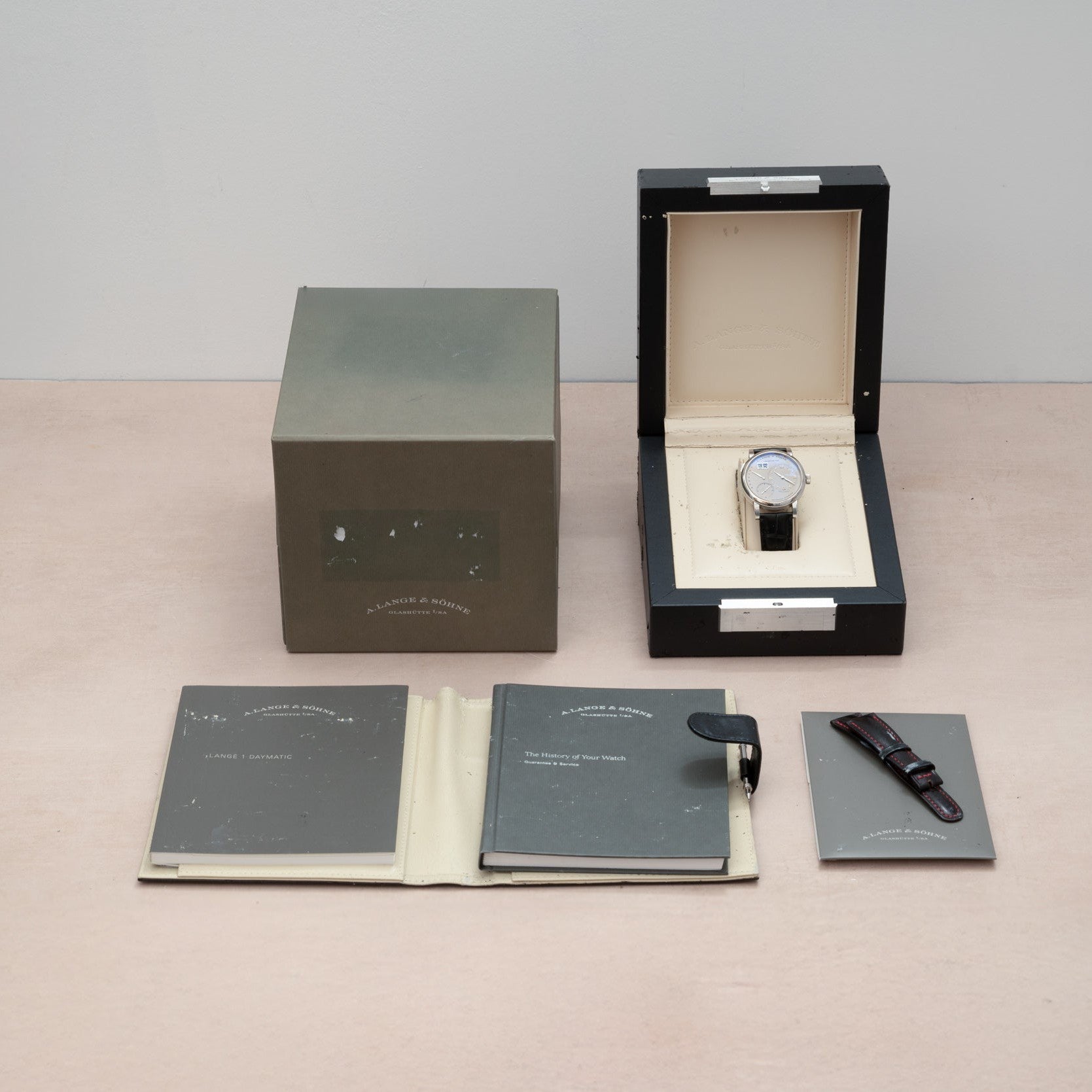 The Lange & Sohne Lange 1 Daymatic comes in its box with outer box, warranty booklets, and an extra strap, all arranged neatly.