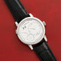 A Lange & Sohne Lange 1 Daymatic wristwatch with a black leather strap rests on a red textured surface.