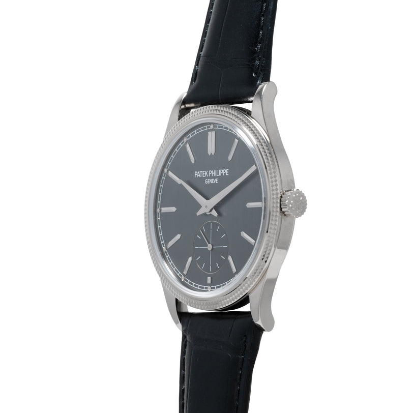 A Patek Philippe Calatrava wristwatch in silver with a black leather strap and dark dial, displayed at an angle.