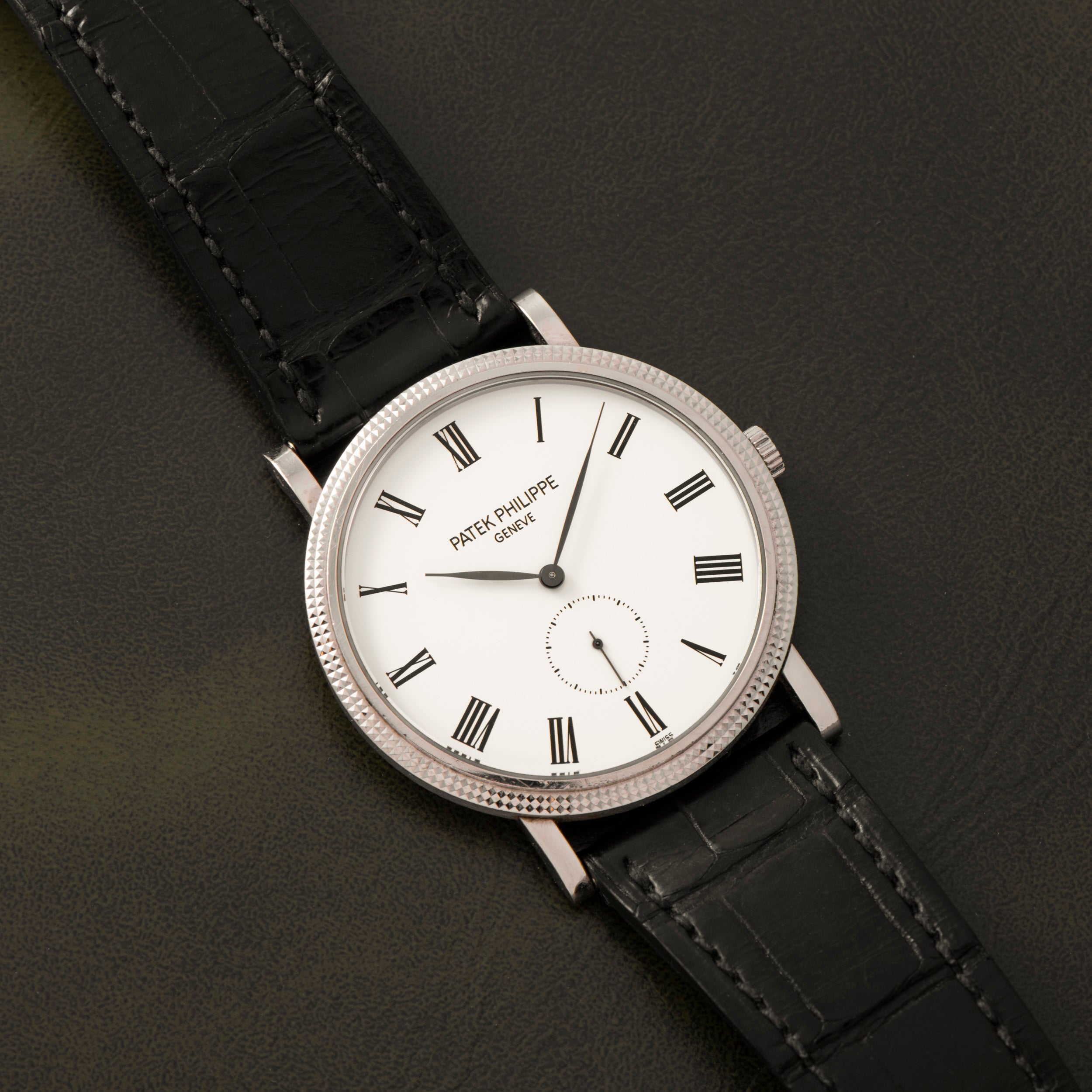 The Patek Philippe Calatrava features a white dial with Roman numerals and a black leather strap.
