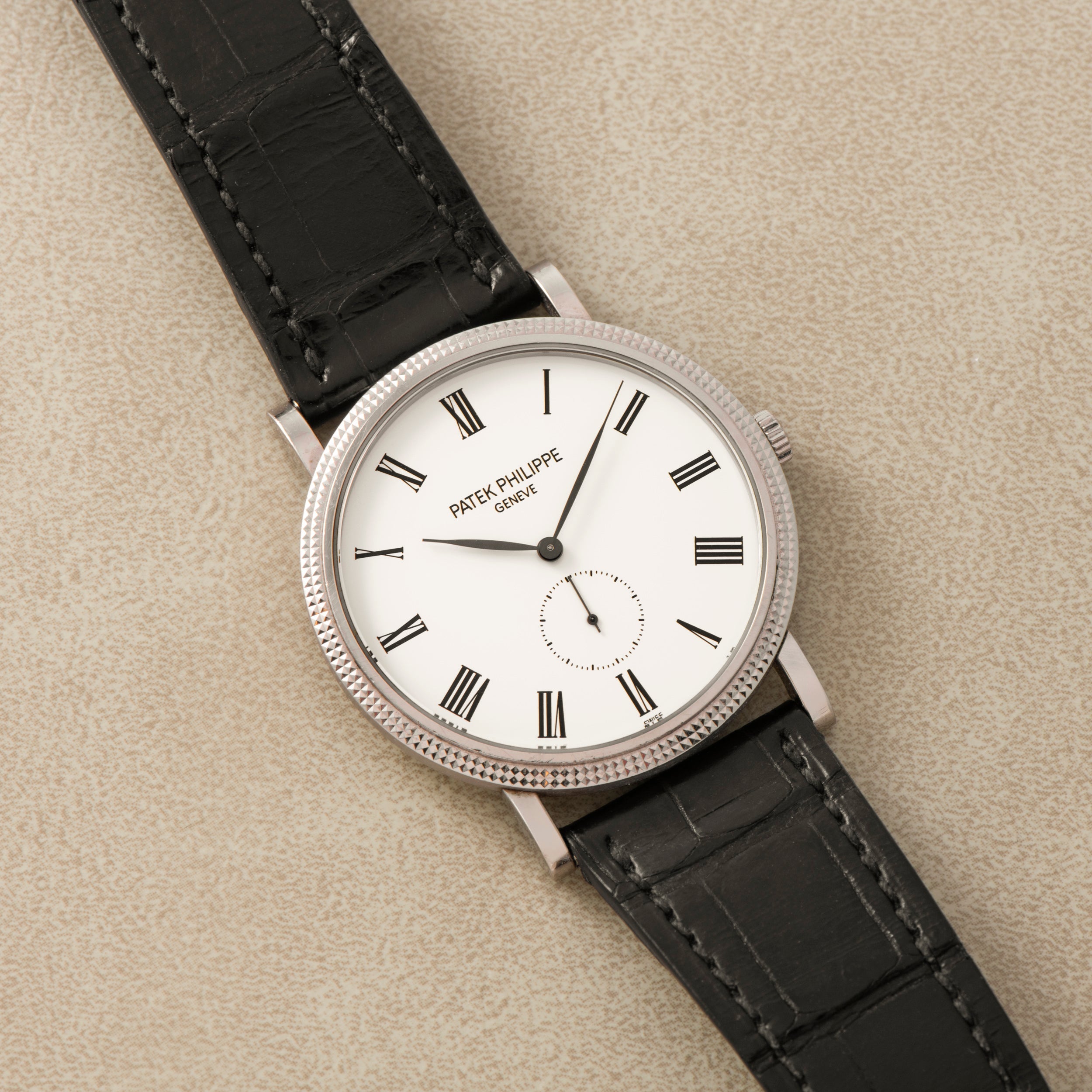 The Patek Philippe Calatrava features a white dial with Roman numerals and a black leather strap.