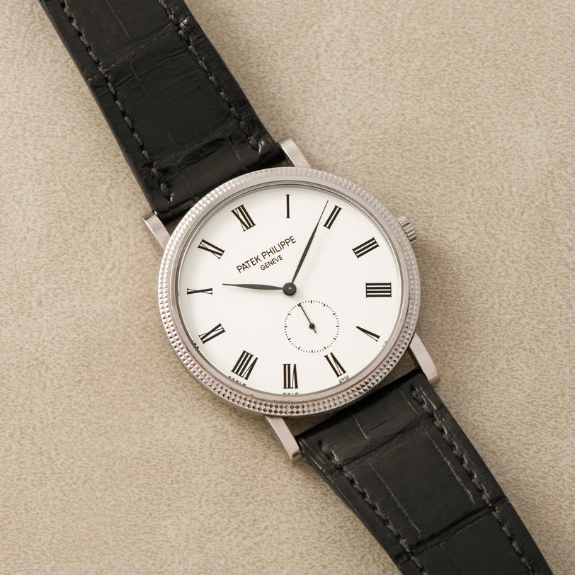 The Patek Philippe Calatrava features a white dial with Roman numerals and a black leather strap.