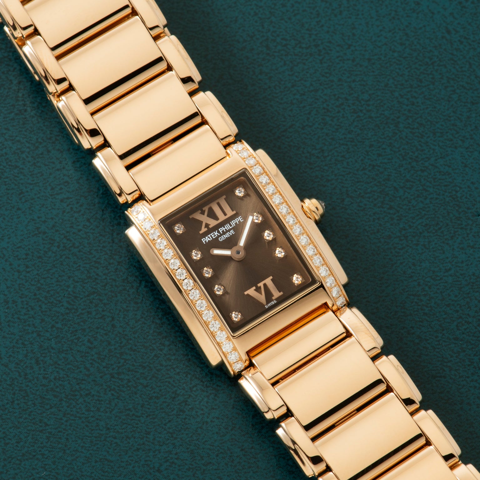 Patek Philippe Twenty-4 gold rectangular wristwatch with diamond accents and black dial displayed on a dark green textured surface.