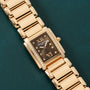Patek Philippe Twenty-4 gold rectangular wristwatch with diamond accents and black dial displayed on a dark green textured surface.