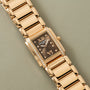 A Patek Philippe Twenty-4 gold watch with diamond accents displayed on a light gray textured surface.