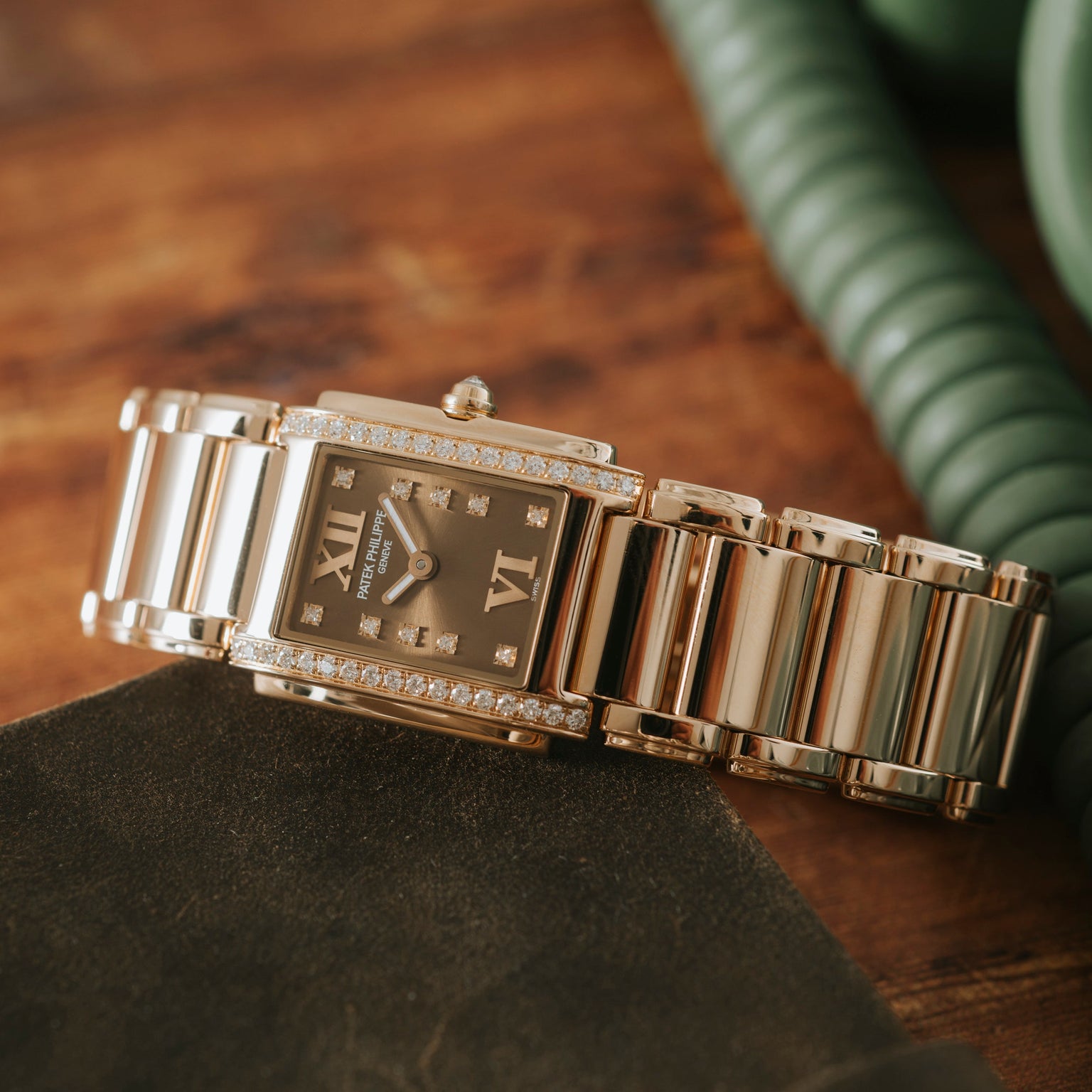The Patek Philippe Twenty-4, a gold and diamond wristwatch with a rectangular face, rests on a brown wooden surface.