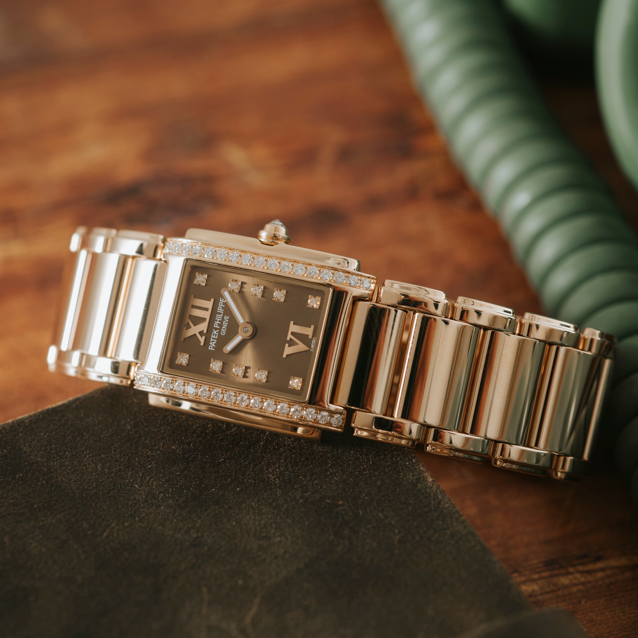 The Patek Philippe Twenty-4, a gold and diamond wristwatch with a rectangular face, rests on a brown wooden surface.