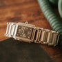 The Patek Philippe Twenty-4, a gold and diamond wristwatch with a rectangular face, rests on a brown wooden surface.
