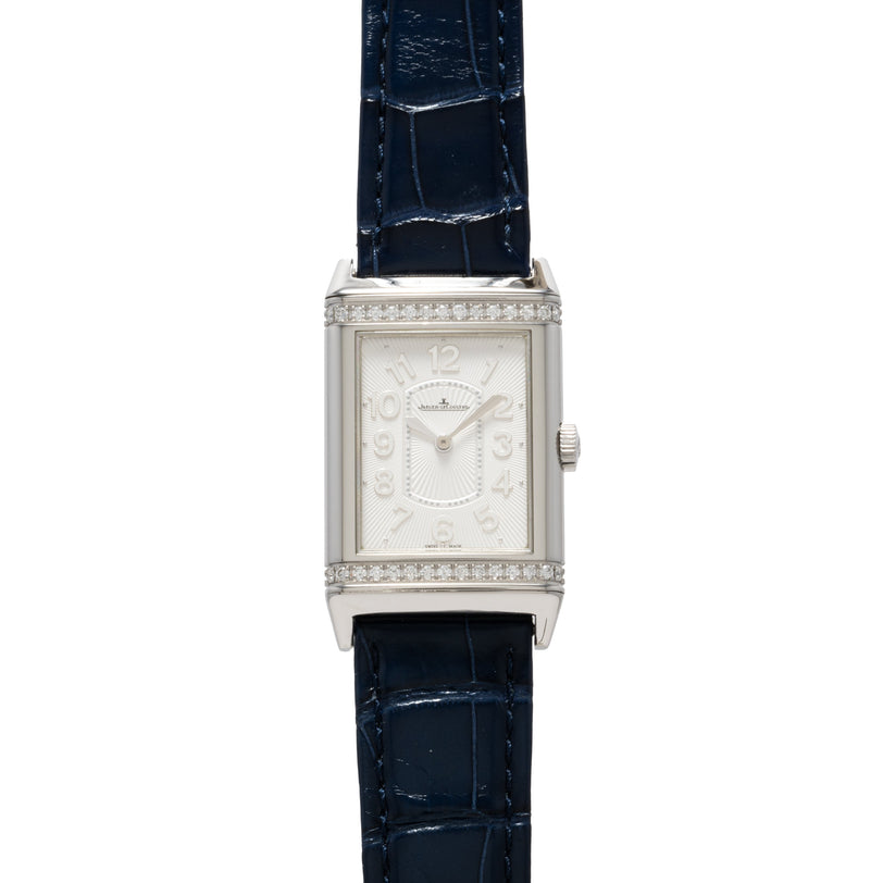 The Jaeger-LeCoultre Reverso Classique Ladies watch features a rectangular silver case, diamond accents, blue leather strap, and displays 12:00 on the dial.