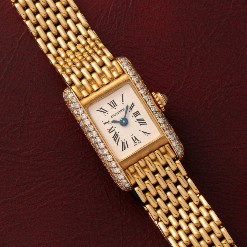 Cartier Tank Louis Mini Diamonds watch with diamond accents displayed on a maroon textured background.