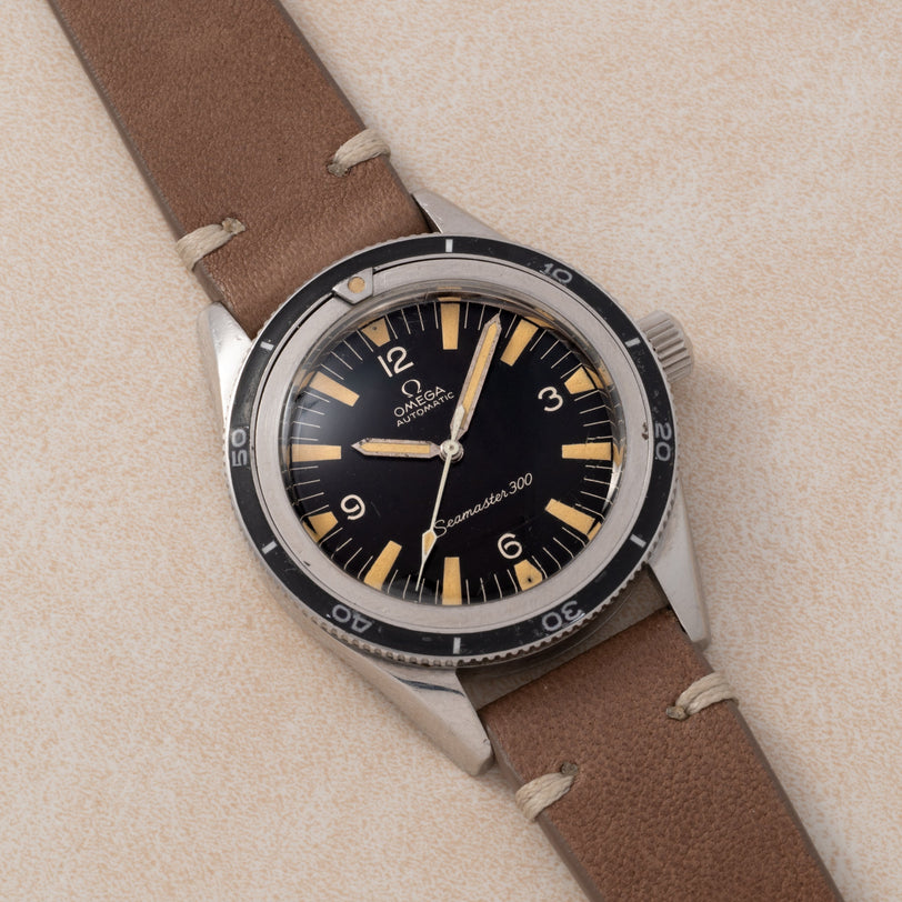 An OMEGA Seamaster 300 watch with a brown leather strap is displayed on a light textured surface.