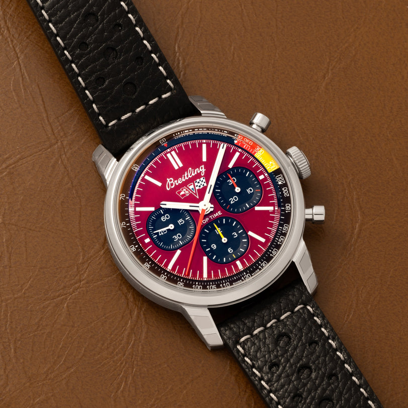 A Breitling Top Time B01 Chronograph Chevrolet Corvette with a red dial and black leather strap, displayed on a brown leather surface.