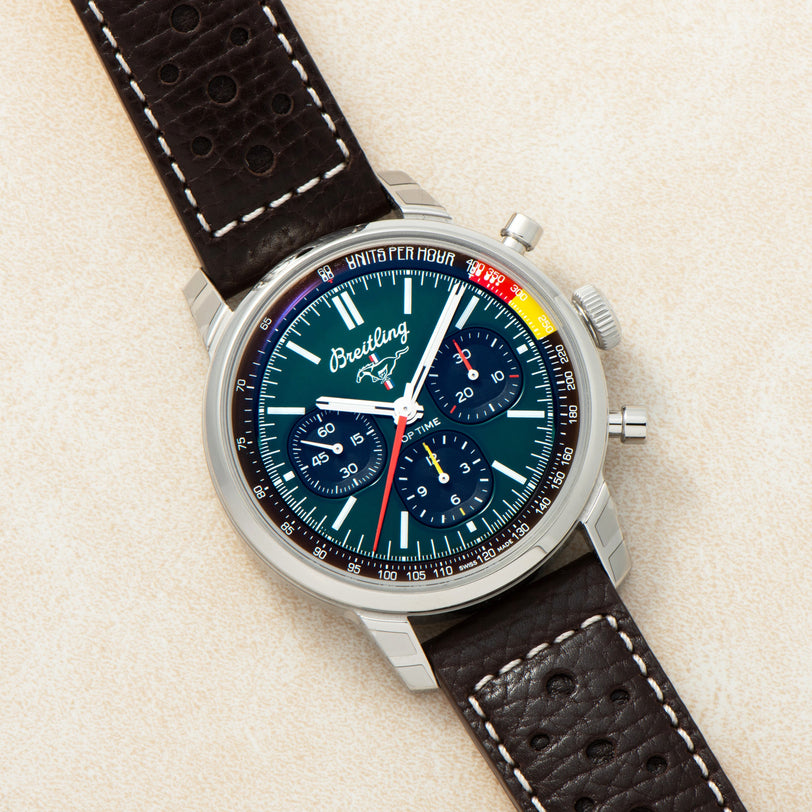 A Breitling Top Time B01 Chronograph Ford Mustang wristwatch featuring a black dial, three subdials, and a brown leather strap is displayed on a light surface.