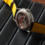 The Breitling Premiere B09 Chronograph 40, a luxury watch with a transparent back and yellow strap, rests on a black leather surface.