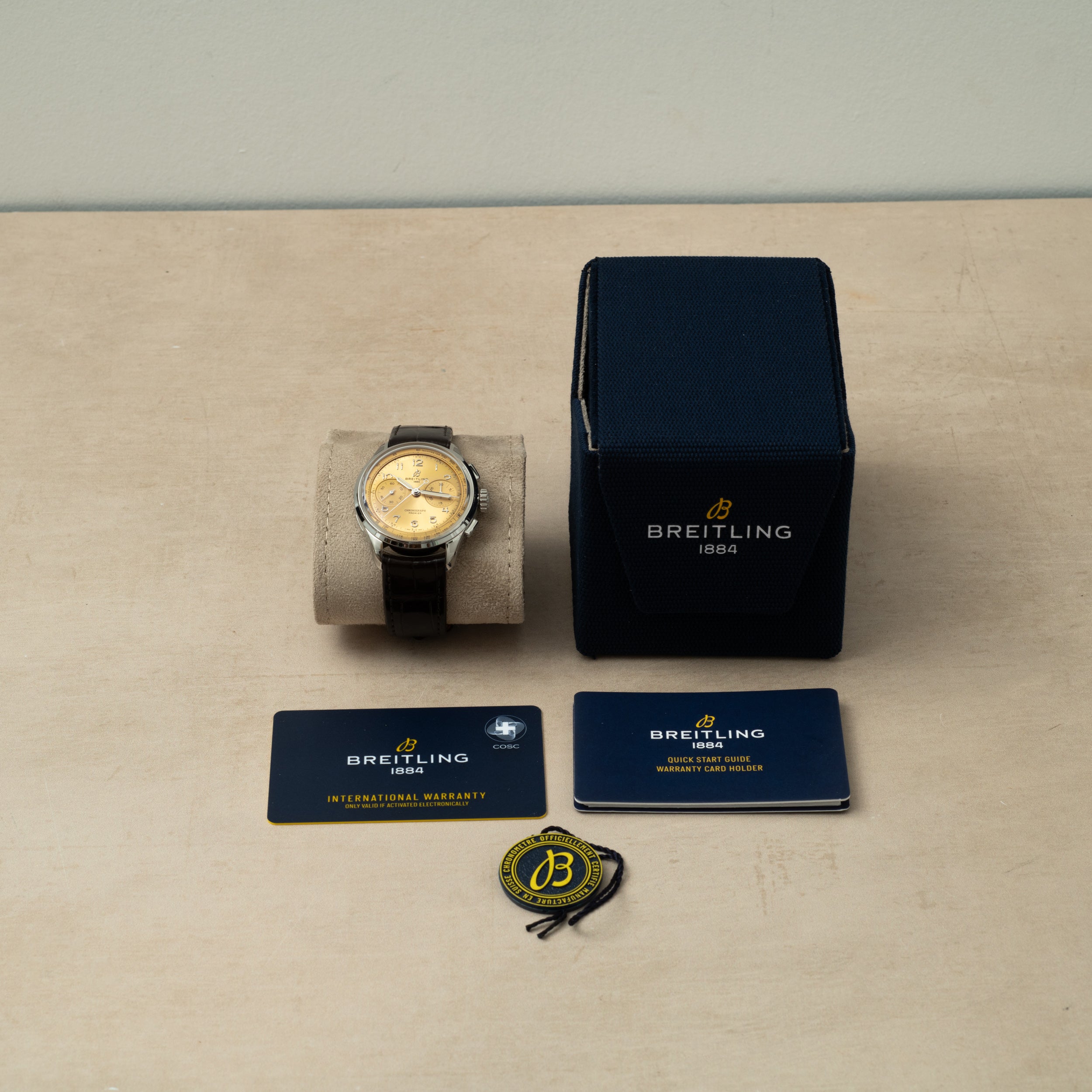 A Breitling Premiere B09 Chronograph 40 with its box, warranty cards, booklet, and tag displayed on a beige surface.