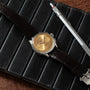 The Breitling Premiere B09 Chronograph 40, featuring a gold face and dark leather strap, is displayed on a black notebook next to a silver pen.