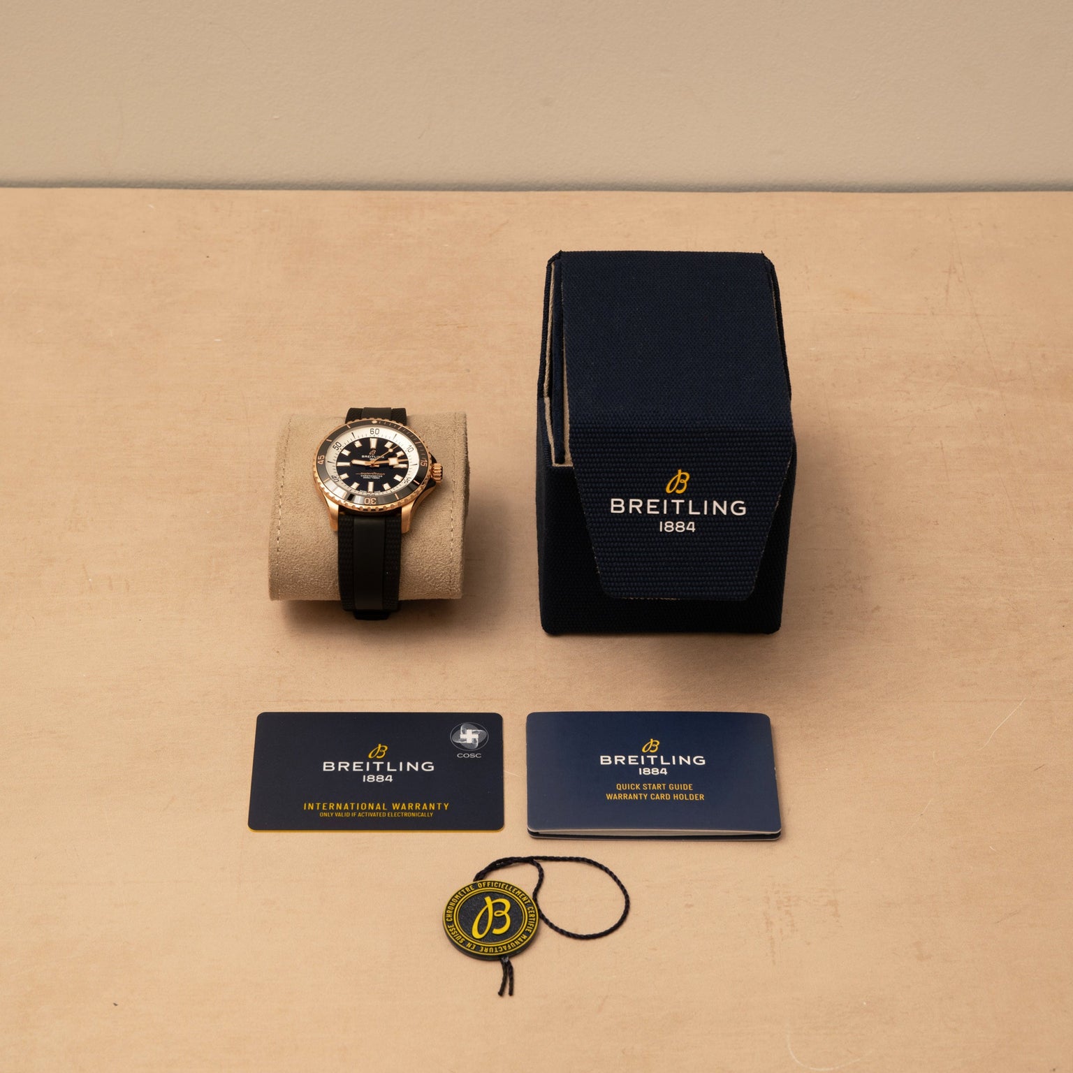 A Breitling Superocean Automatic 42 with box, warranty cards, and branded tag displayed on a beige surface.
