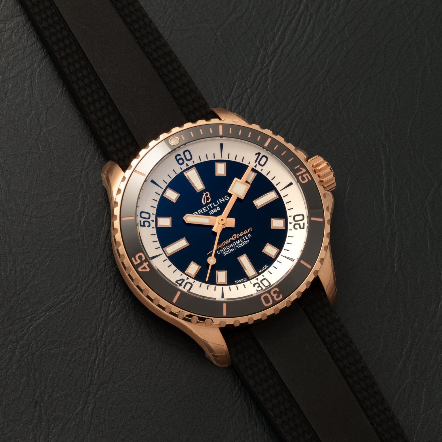 A Breitling Superocean Automatic 42 gold dive watch with a black strap, blue dial, and white bezel displayed on dark leather.