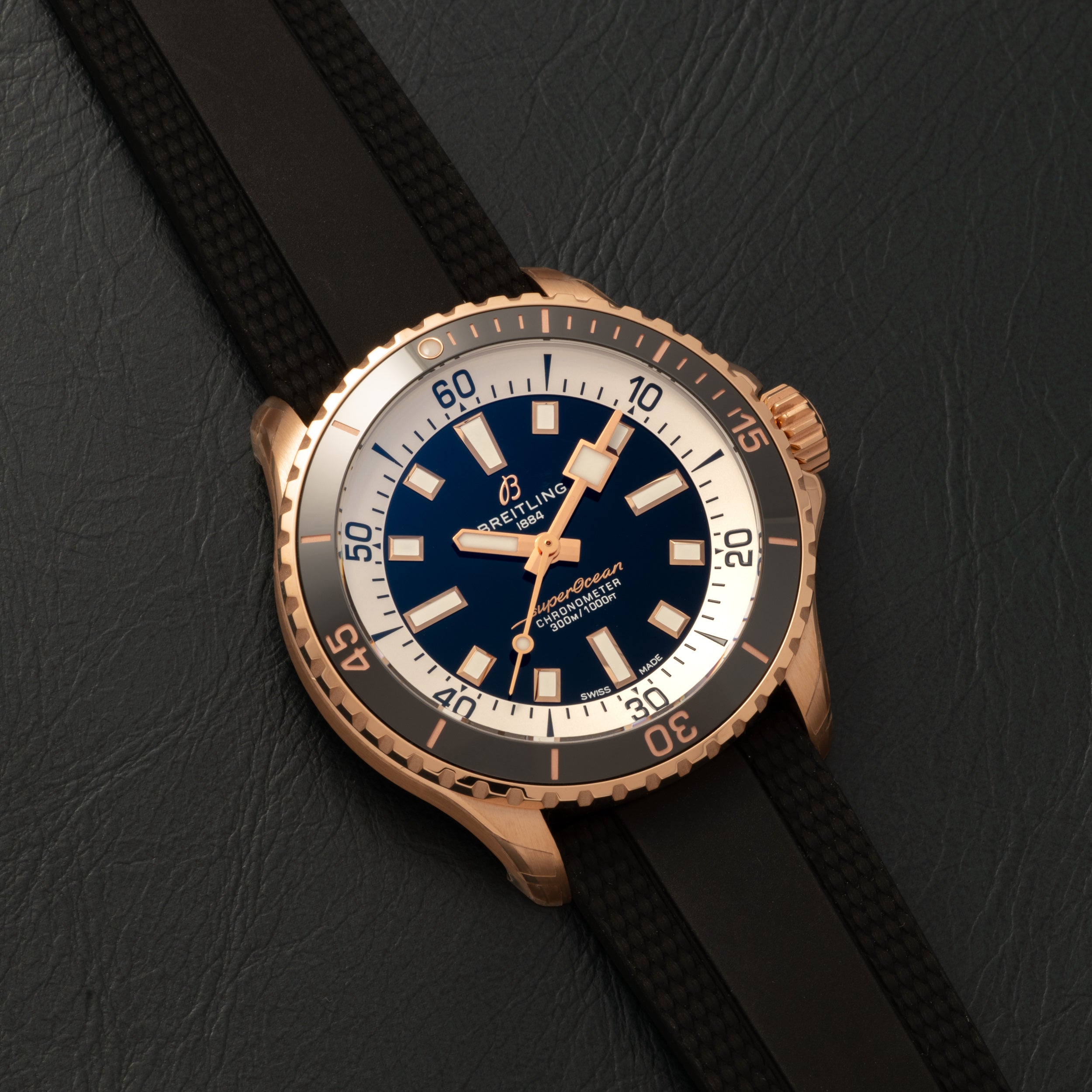A Breitling Superocean Automatic 42 gold dive watch with a black strap, blue dial, and white bezel displayed on dark leather.