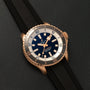 A Breitling Superocean Automatic 42 gold dive watch with a black strap, blue dial, and white bezel displayed on dark leather.