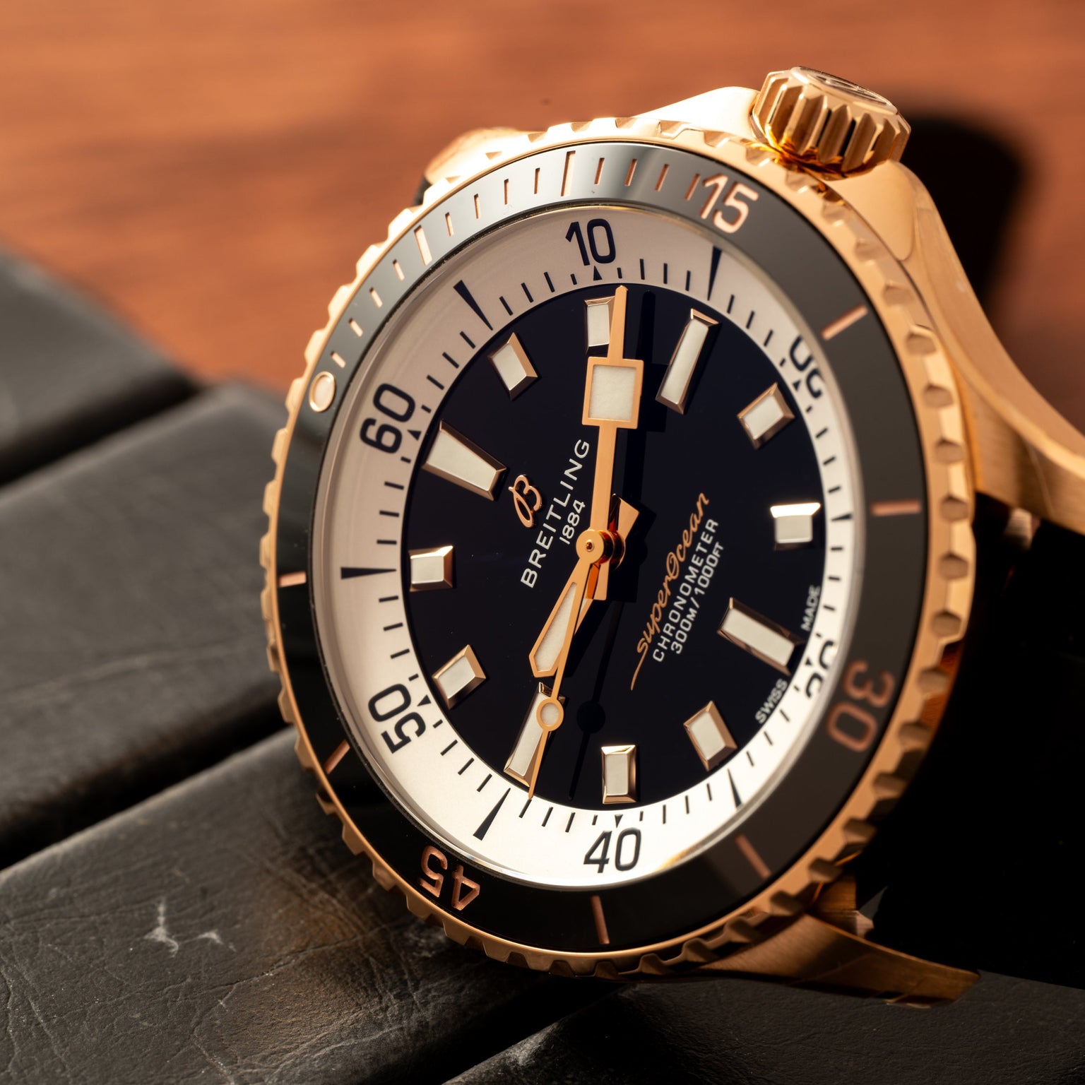 Close-up of the Breitling Superocean Automatic 42, a gold dive watch featuring a black dial with white accents, resting on a black surface.