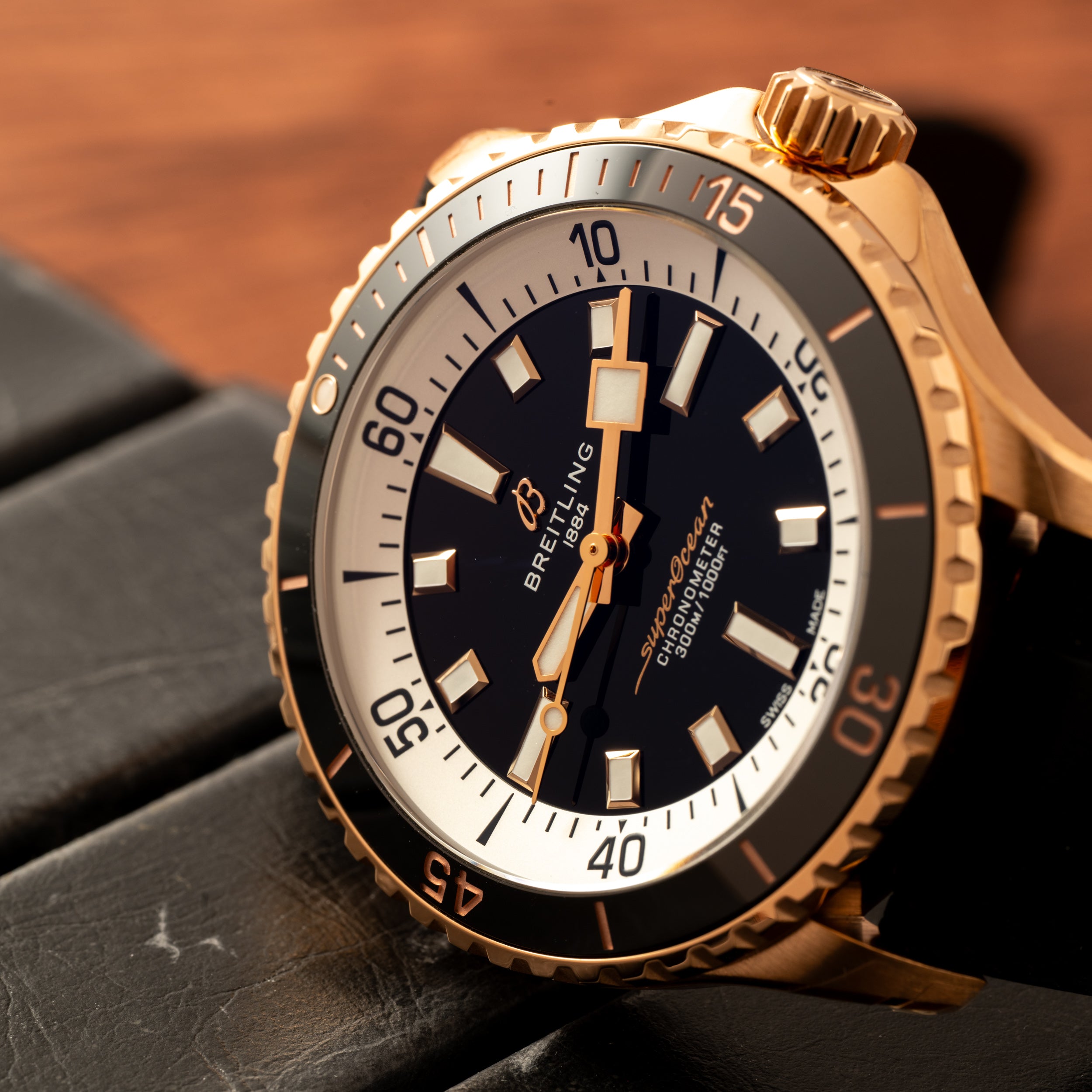 Close-up of the Breitling Superocean Automatic 42, a gold dive watch featuring a black dial with white accents, resting on a black surface.