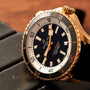 Close-up of the Breitling Superocean Automatic 42, a gold dive watch featuring a black dial with white accents, resting on a black surface.