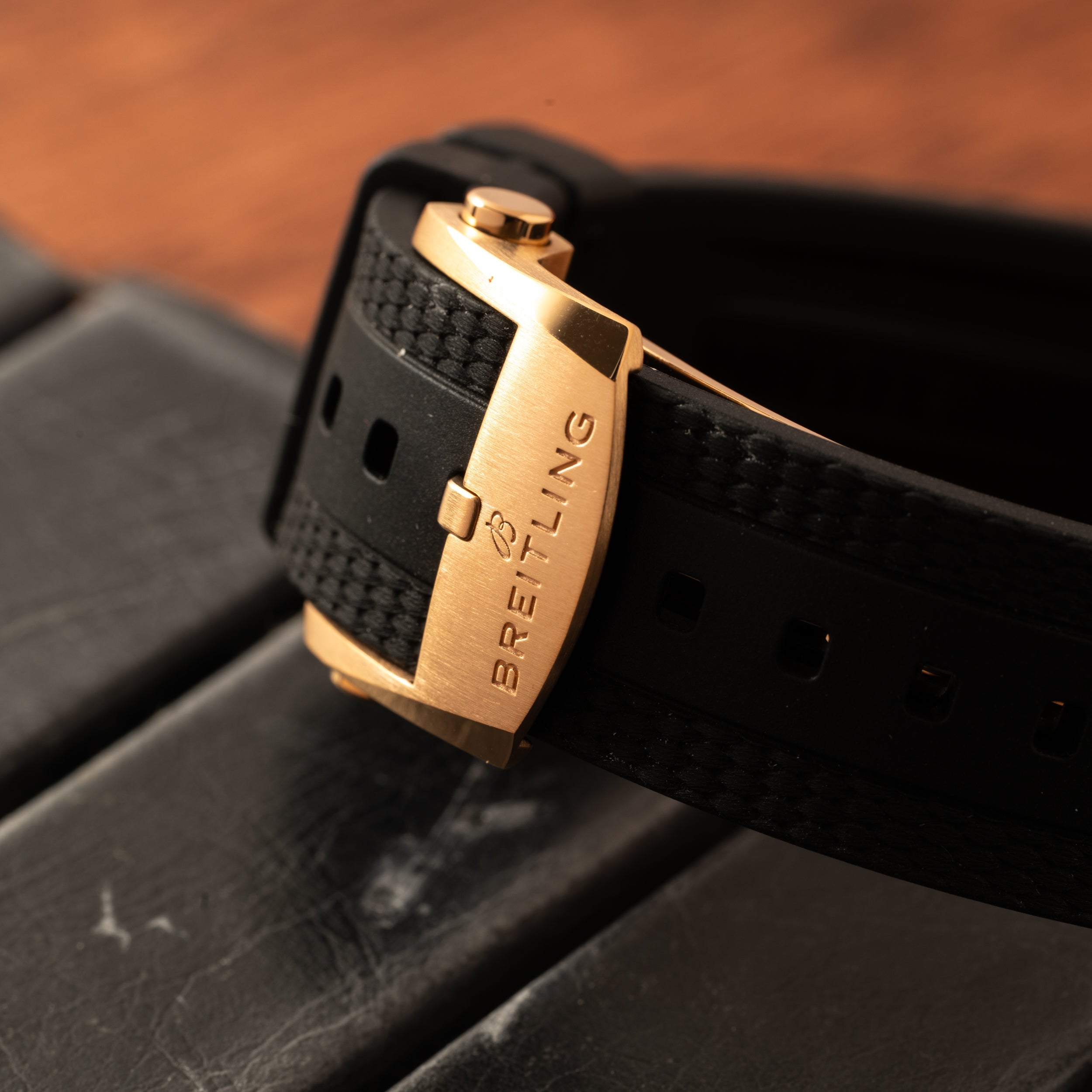 Close-up of a gold Breitling Superocean Automatic 42 clasp on a black rubber strap, resting on a dark surface.