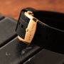 Close-up of a gold Breitling Superocean Automatic 42 clasp on a black rubber strap, resting on a dark surface.