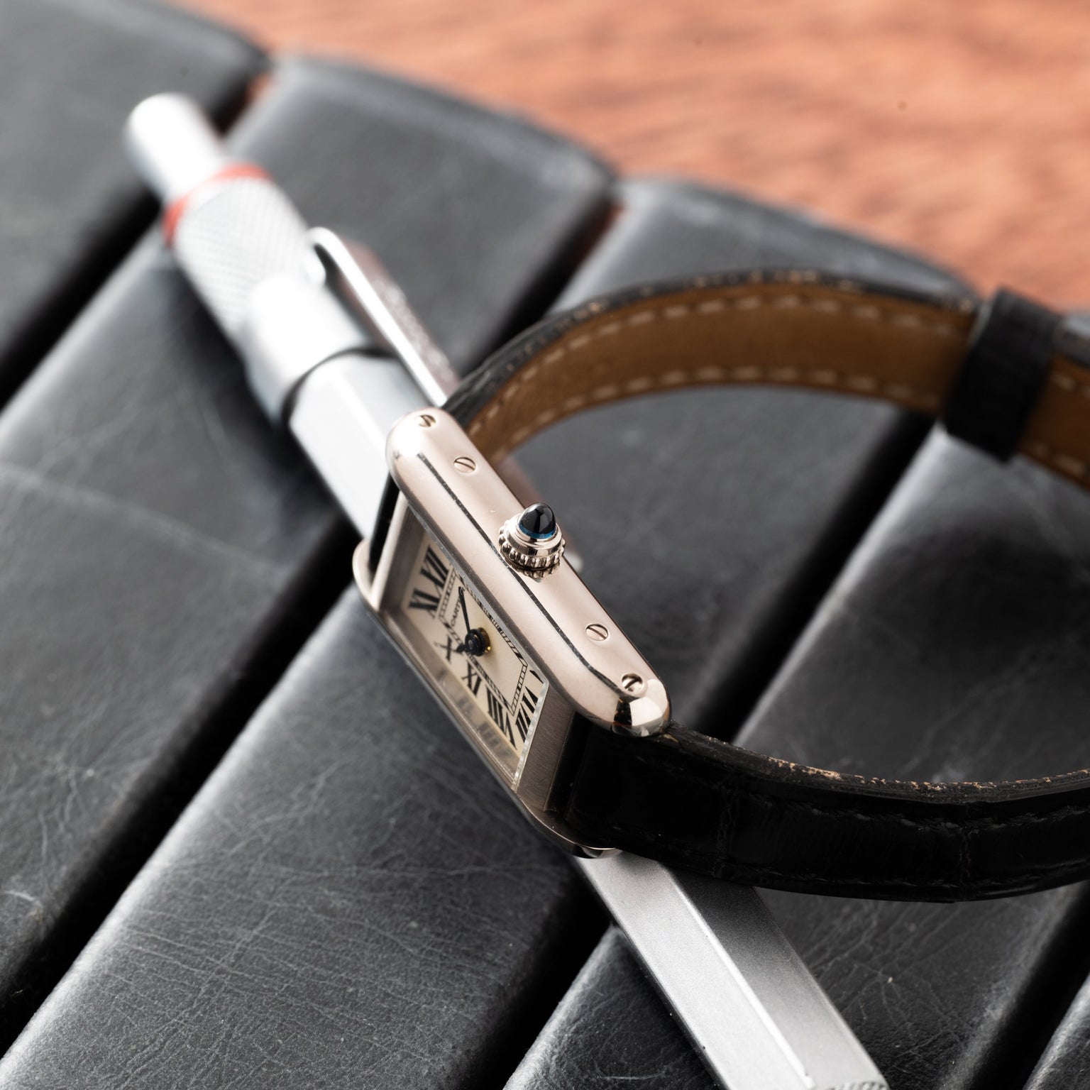 The Cartier Tank Ladies Allongee luxury wristwatch with a black leather strap rests on a pen and a black leather notebook.
