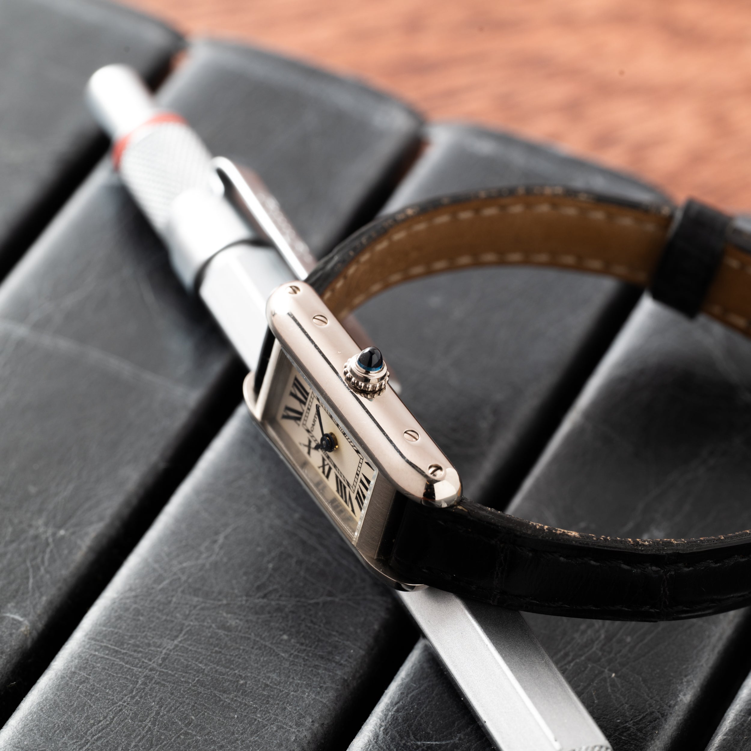 The Cartier Tank Ladies Allongee luxury wristwatch with a black leather strap rests on a pen and a black leather notebook.