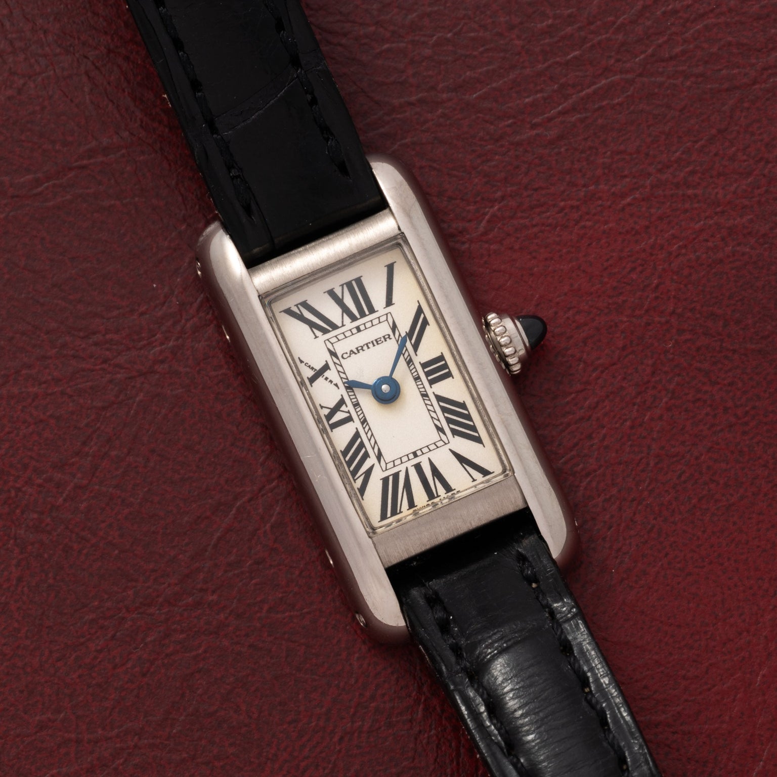 The Cartier Tank Ladies Allongee features a rectangular case, Roman numerals, and a black leather strap, displayed on a red textured surface.