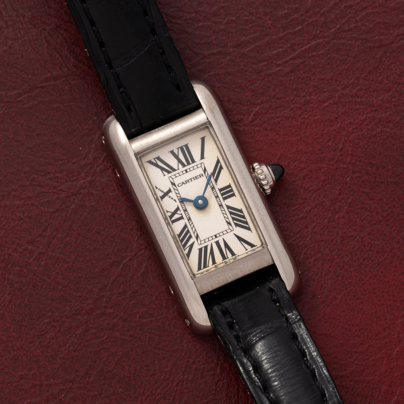 The Cartier Tank Ladies Allongee features a rectangular case, Roman numerals, and a black leather strap, displayed on a red textured surface.