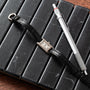 A Cartier Tank Ladies Allongee watch with a black leather strap and a silver pen placed on a black notebook.