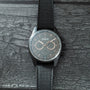 Zenith chronograph watch with dark gray dial, three subdials, date window, and black textile strap on textured surface.